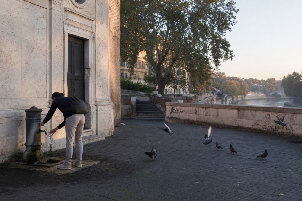 A visitor refilling a water bottle at a public drinking fountain beside a Rome church facade