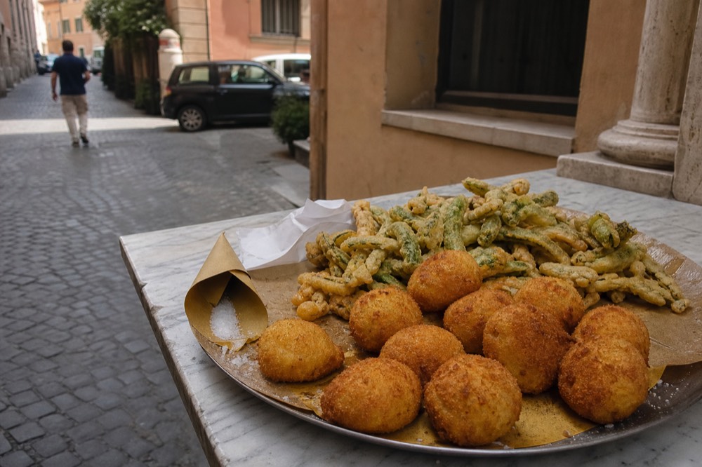 Fried rice croquettes and fried vegetables arranged on a market counter