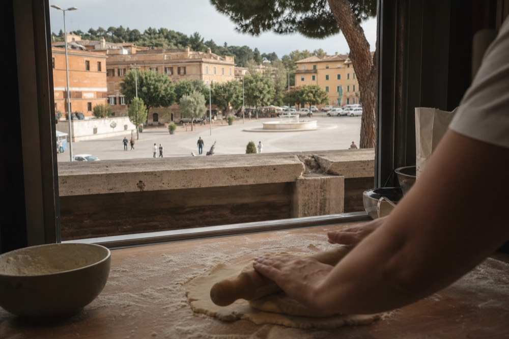 Fresh pasta dough being rolled with a rolling pin on a floured wooden board