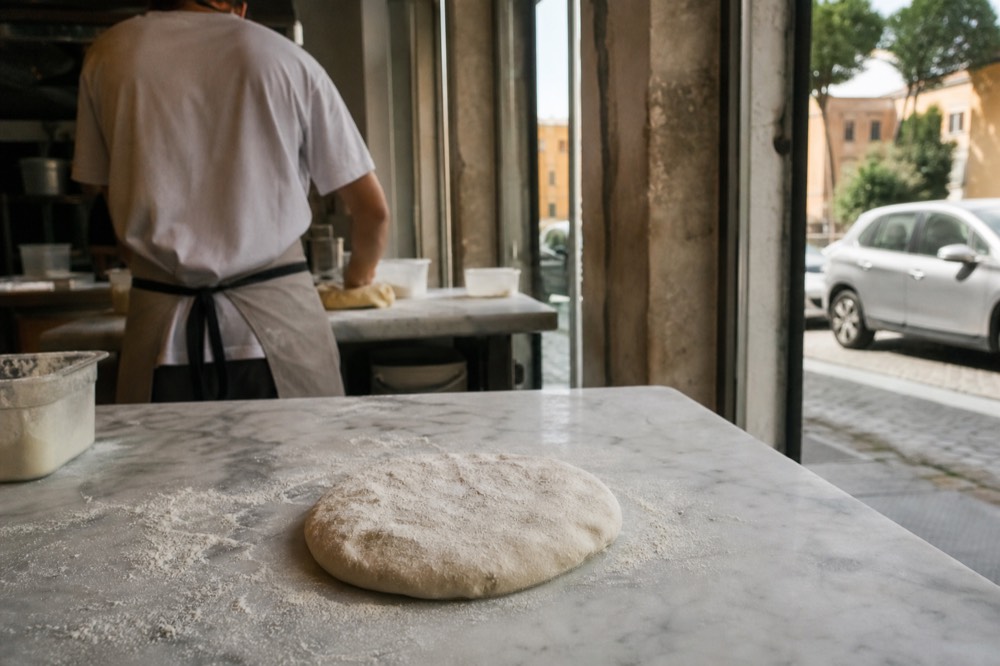 Hands shaping pizza dough on a marble work surface in a cooking school