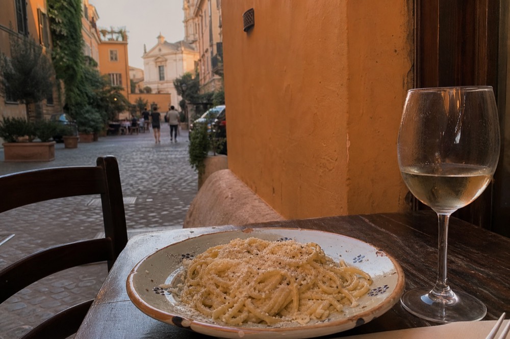 A plate of fresh pasta with cheese and pepper beside a glass of white wine