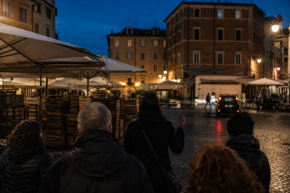 A guide speaking to a small group on a Rome street at dusk