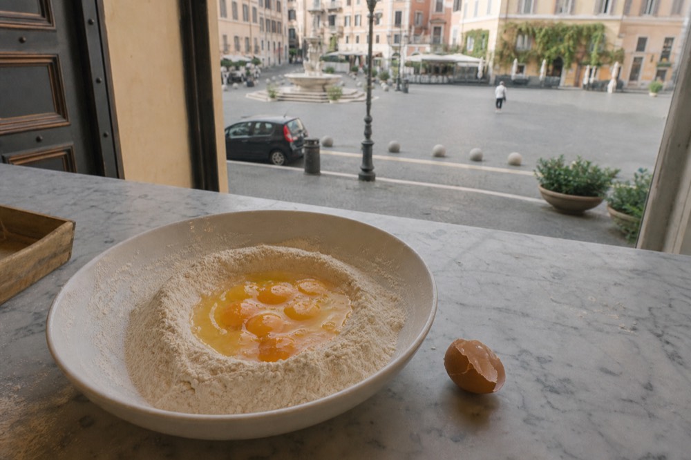 A mound of flour with whole eggs cracked into a well in the center, ready to be mixed into pasta dough