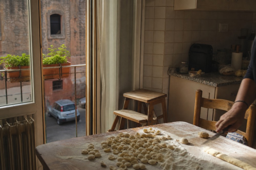 Hands pressing small balls of pasta dough into orecchiette shapes on a wooden table