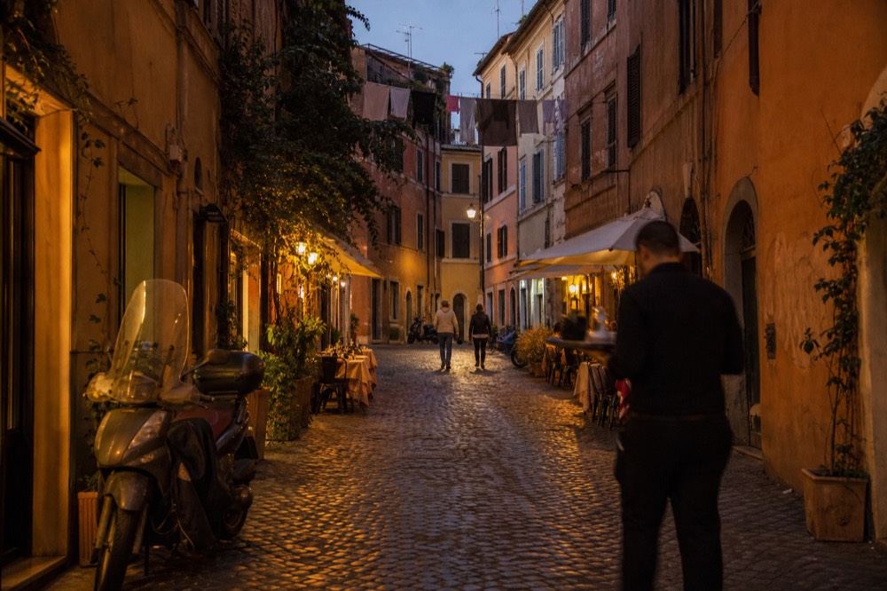 Cobbled Trastevere street at dusk with restaurant tables and warm lights