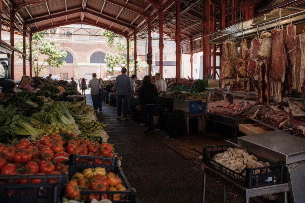Market stalls with produce and shoppers under the roof of a Roman market hall