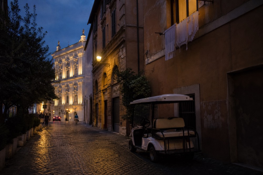 Golf cart parked on a Roman street near an illuminated building at dusk