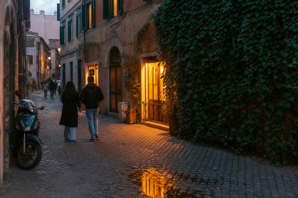 Evening street in Trastevere with lit shopfronts and people walking