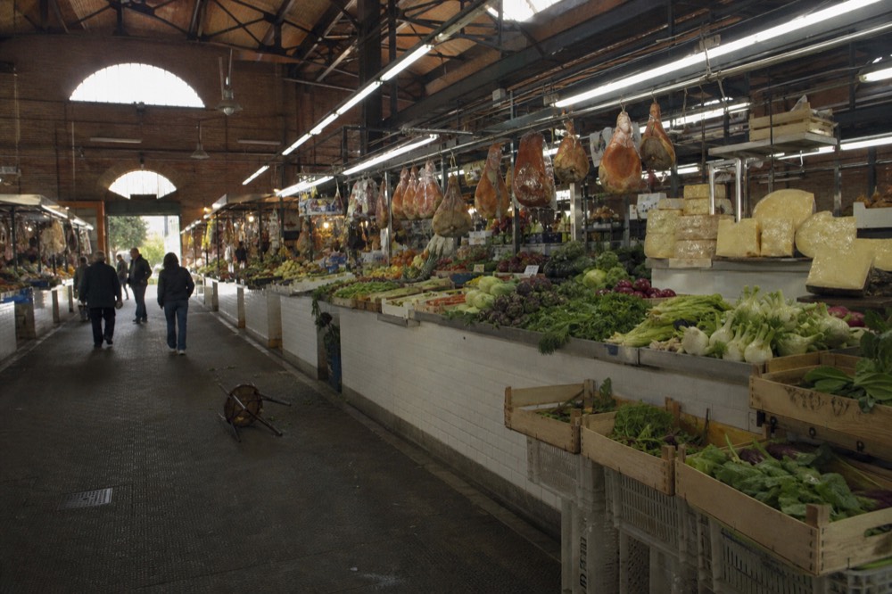 Interior of a covered market hall with stalls of vegetables, cheese and cured meats under bright lights