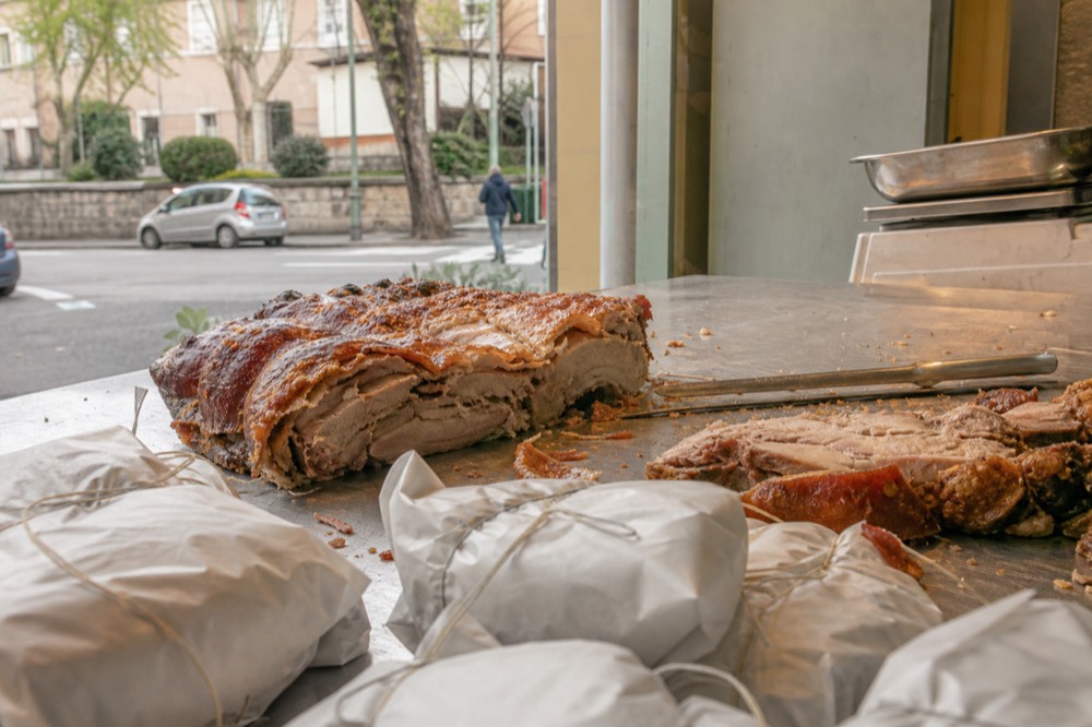 Close view of a market counter with sliced porchetta and paper-wrapped portions