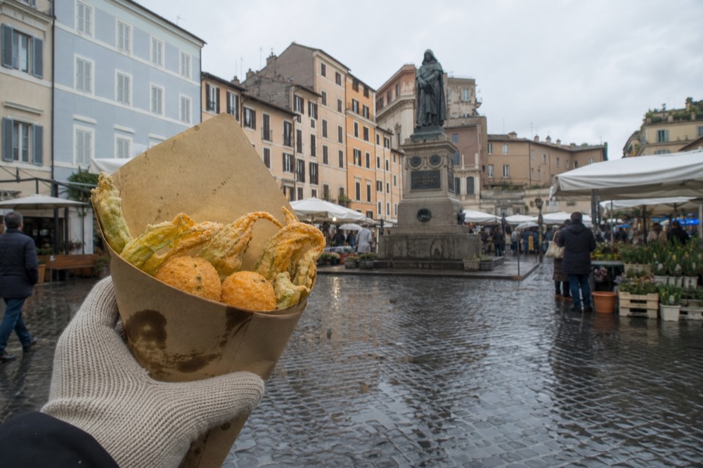 Fried vegetable snacks and rice croquettes in a paper cone held in hand