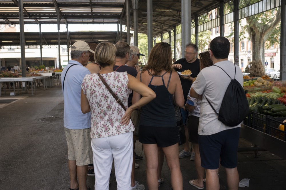 Small group of visitors sampling food from a market stall with a guide