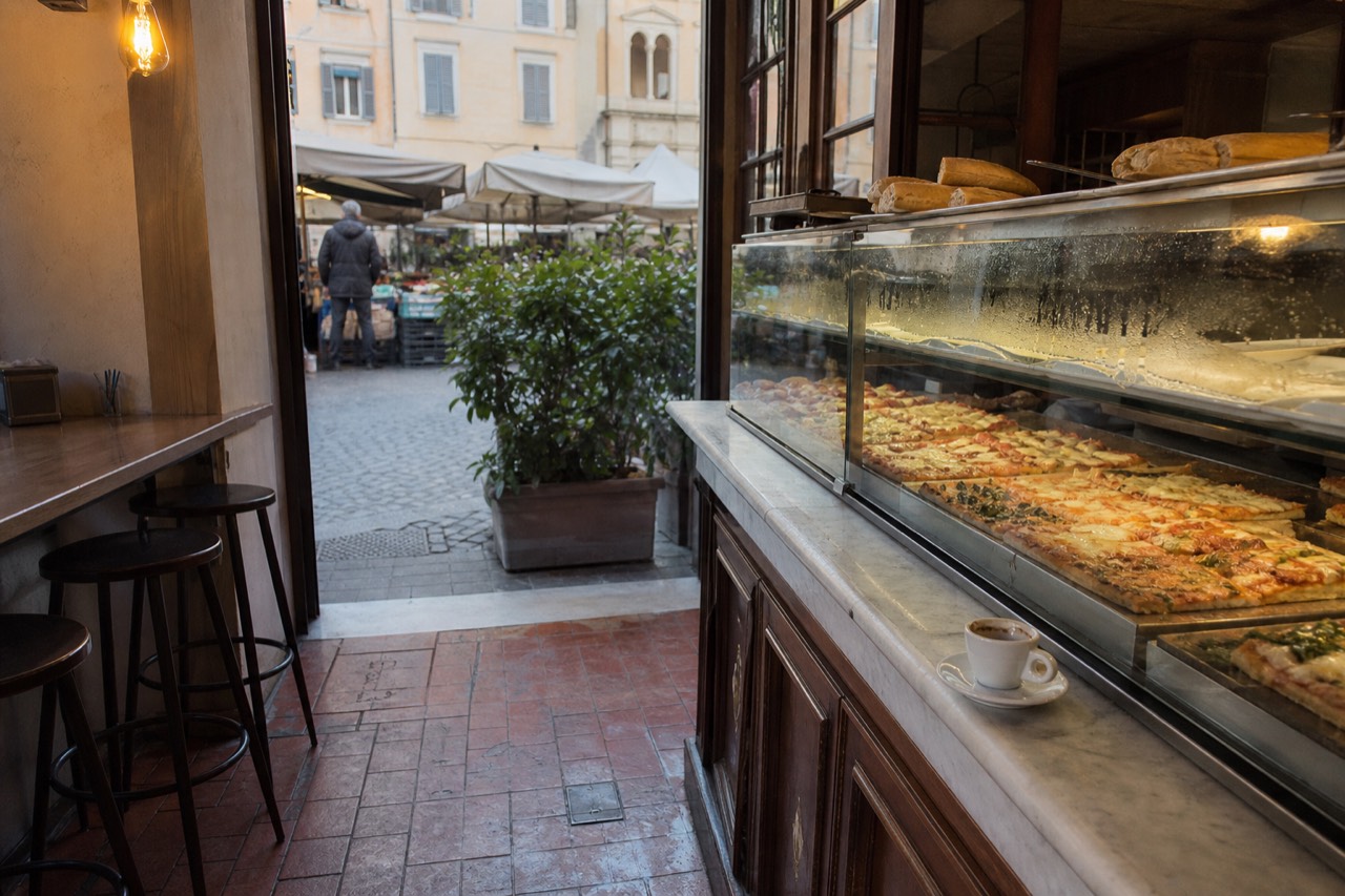 Sliced rectangular pizza displayed in a glass counter at a Roman bakery