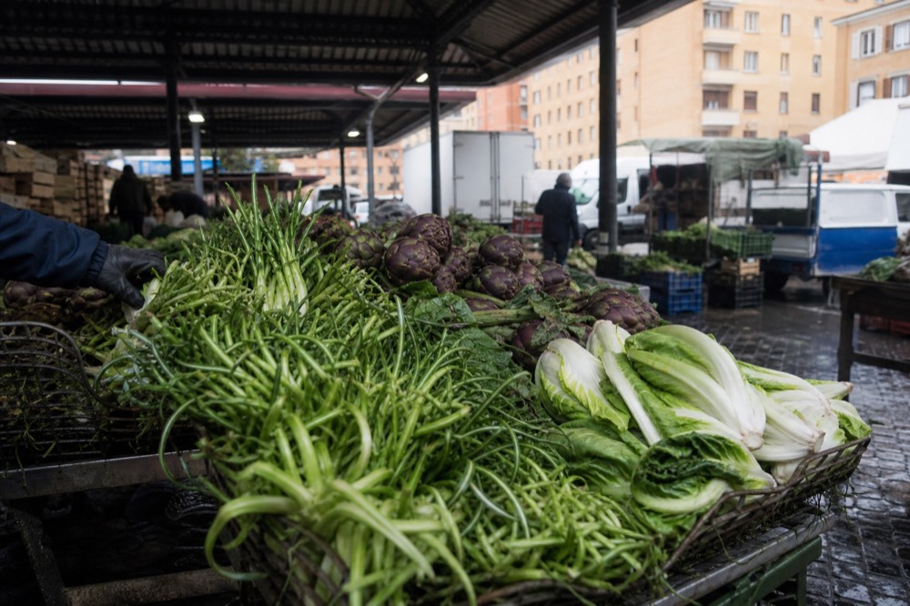 Market stall with artichokes and leafy greens under a covered hall