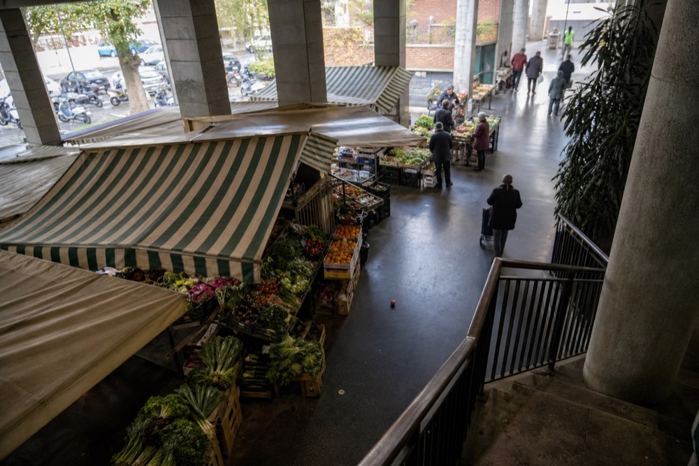 Interior of a covered market with stall awnings and shoppers at produce stands