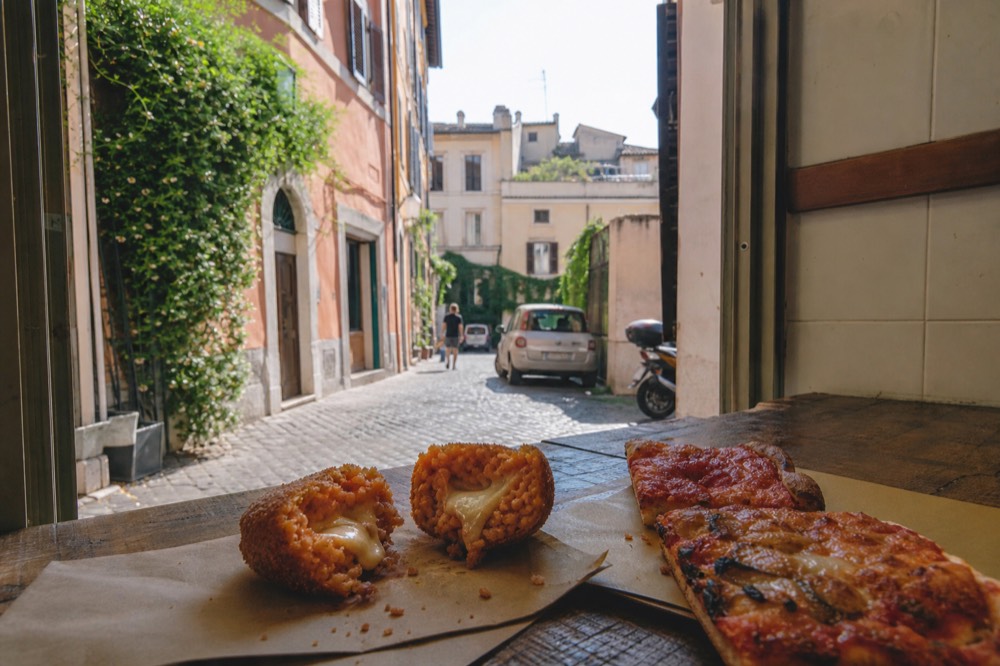 Supplì and pizza al taglio arrayed on a Trastevere counter, no text, no logos, no people