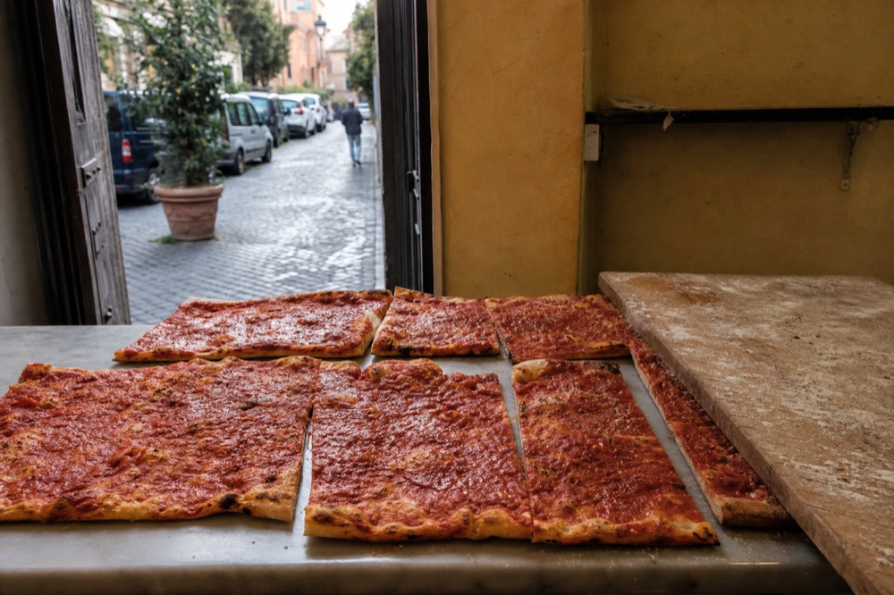Rectangles of Roman pizza rossa with tomato topping displayed on a bakery counter