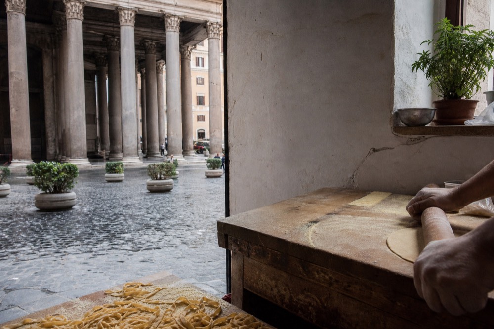 Hands rolling fresh pasta dough on a wooden board in a cooking school