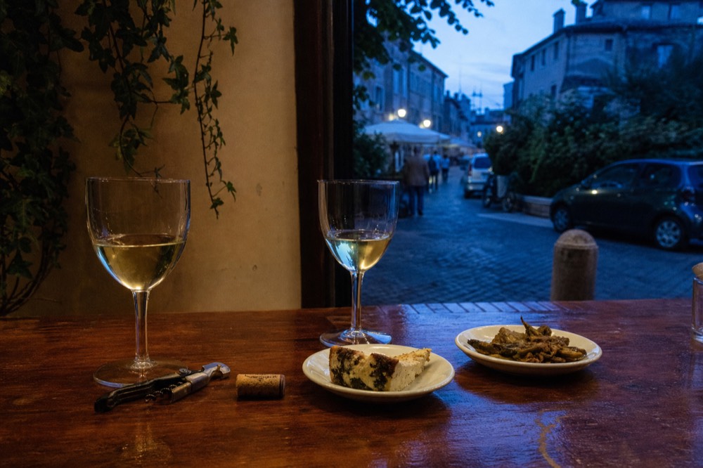 Small plates and glasses of wine arranged on a wooden counter in a Roman enoteca