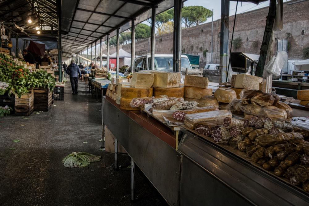 Stalls of a covered Roman food market with produce, cheese and cured meats on display