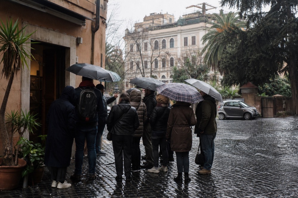 A tour guide speaking to a small group outside a small Roman food shop