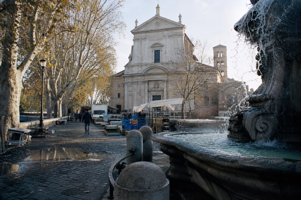 A fountain in a Roman square in the morning with market stalls nearby