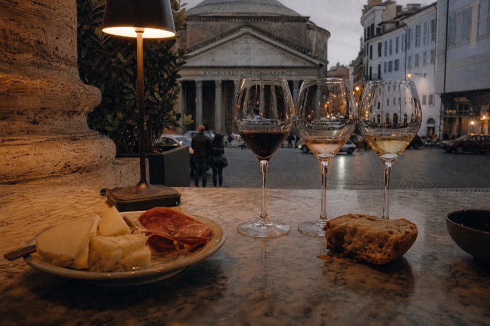 A flight of three wine glasses beside a plate of cheese and cured meats on a marble counter