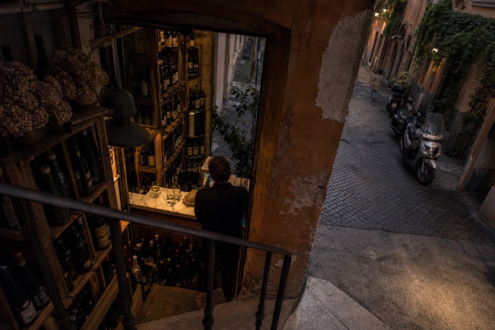 A narrow enoteca interior with bottles stacked along the walls and a small tasting counter