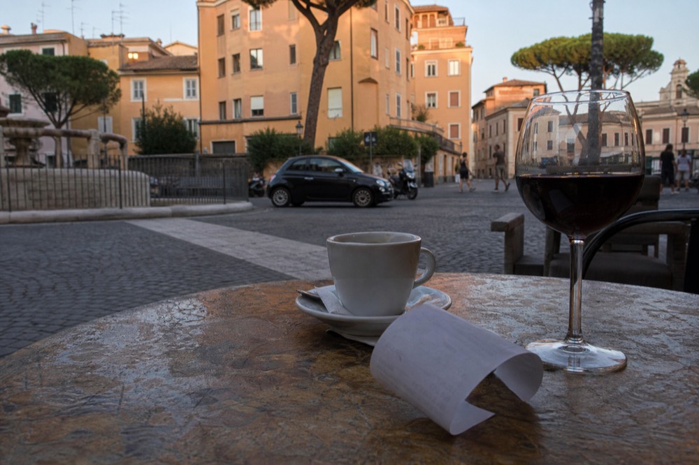 A receipt and a glass of red wine on a cafe table in a Roman piazza