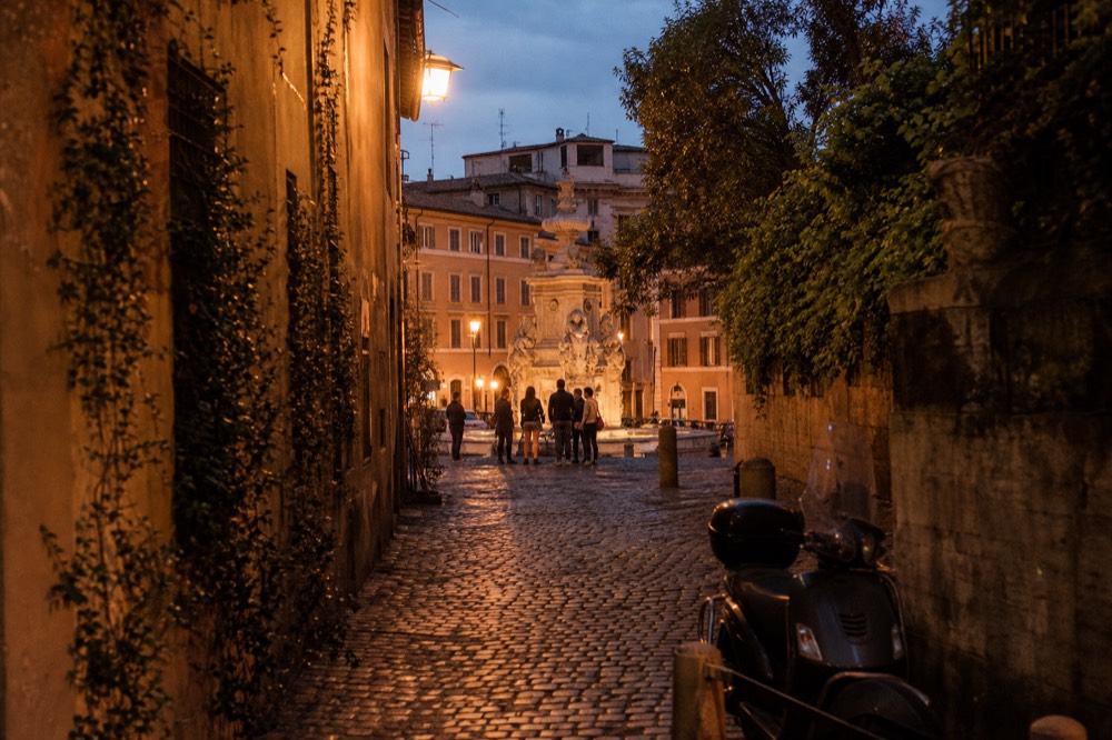A guide with a small group holding wine glasses in a cobbled evening street in Rome
